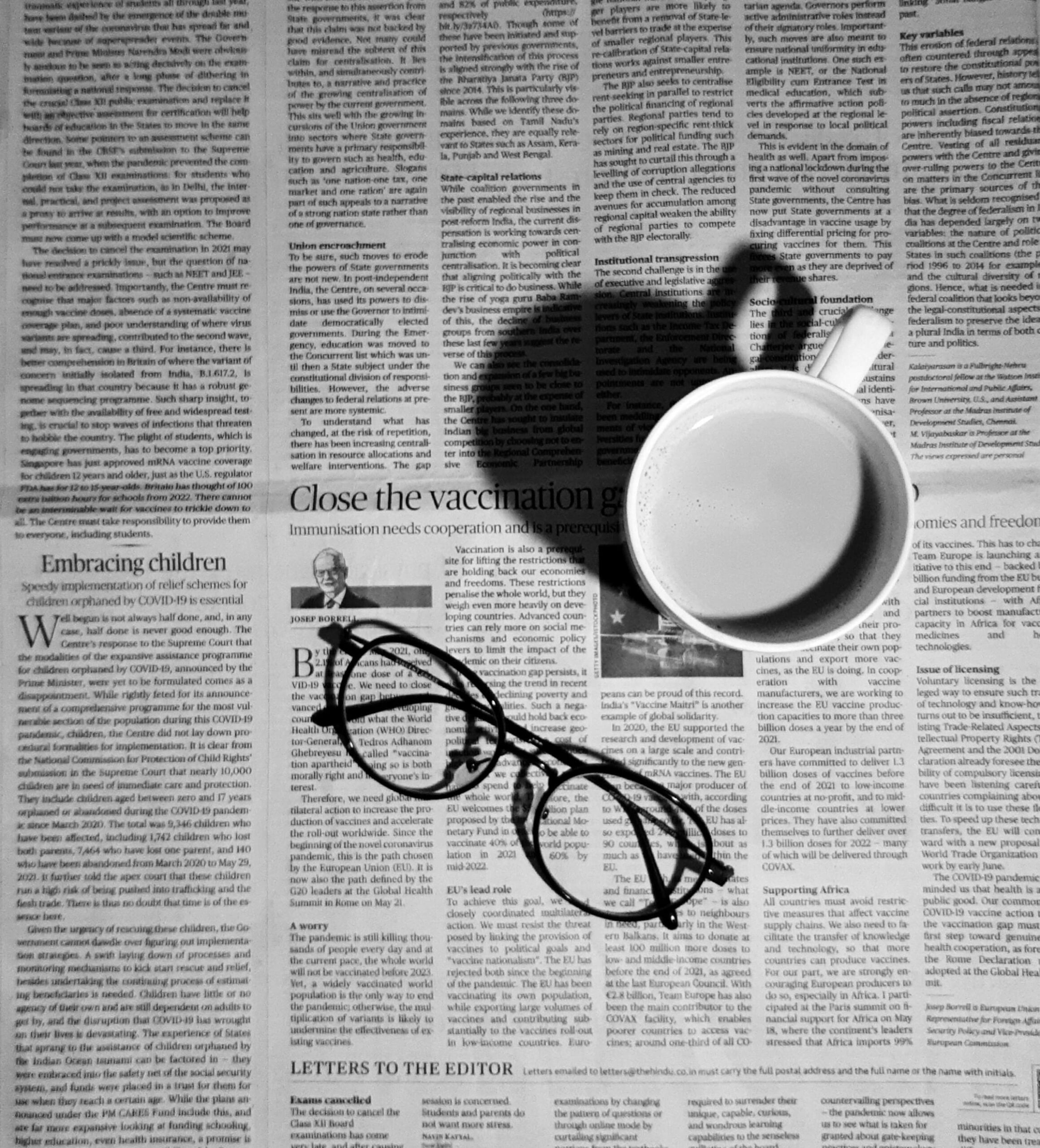 A coffee mug and pair of reading glasses on top on a newspaper.